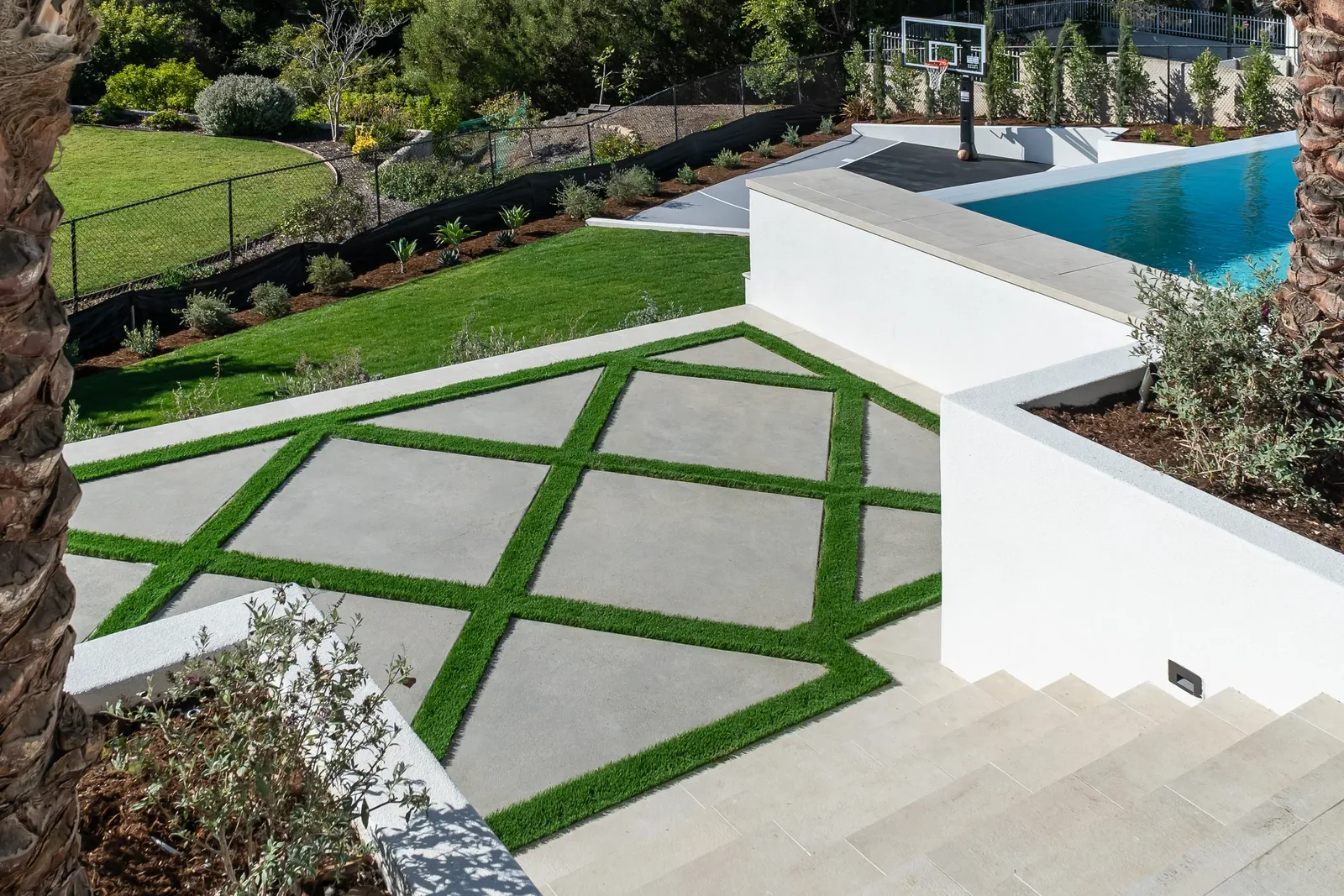 Hillside estate with geometric turf-and-concrete patio, pool and sport court