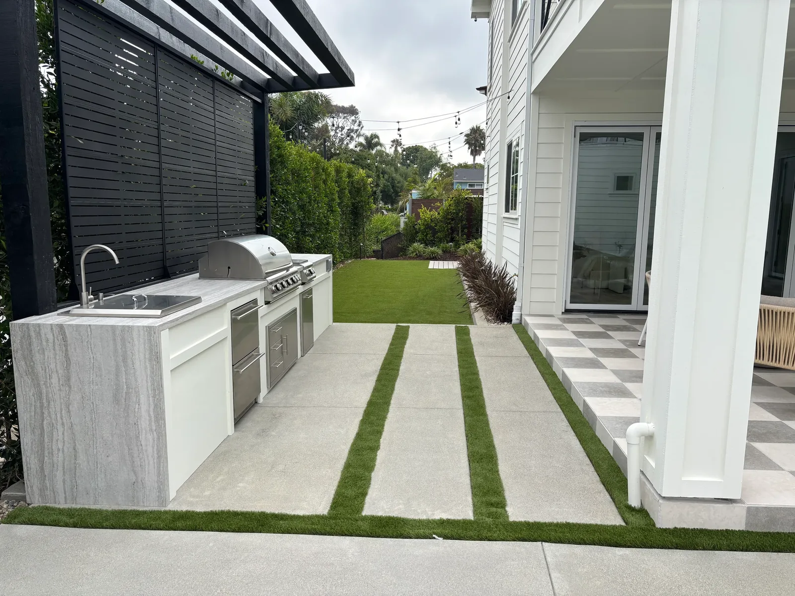 Coastal modern farmhouse backyard with outdoor kitchen, turf ribbons and checkerboard patio